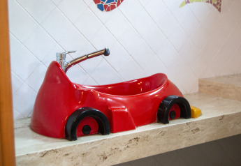 Lavabo a forma di auto rossa in un bagno di una struttura glamping, su un piano in marmo beige.