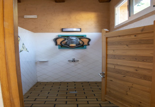 Doccia in un alloggio glamping con porta in legno, piastrelle bianche e decorazione testa di elefante.