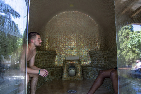 Dos personas se relajan en un baño de vapor con azulejos de mosaico en un alojamiento de glamping rodeado de naturaleza.
