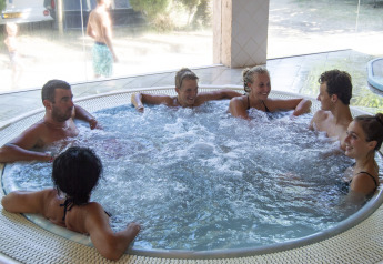 Un gruppo di persone si rilassa in una vasca idromassaggio interna in una struttura glamping immersa nella natura.