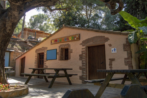 Zona esterna con panche di legno davanti a una mini club house per bambini in un campeggio di glamping.