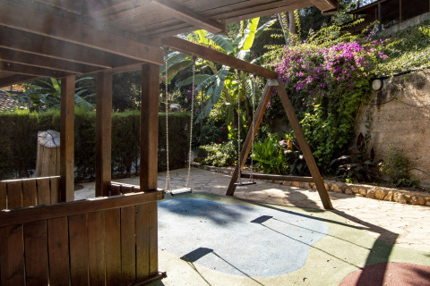Parque infantil con columpio y casa de madera en un glamping, rodeado de un jardín exuberante.