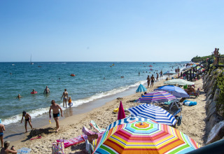 Ombrelloni colorati e persone che godono la spiaggia vicino al mare durante un soggiorno glamping.