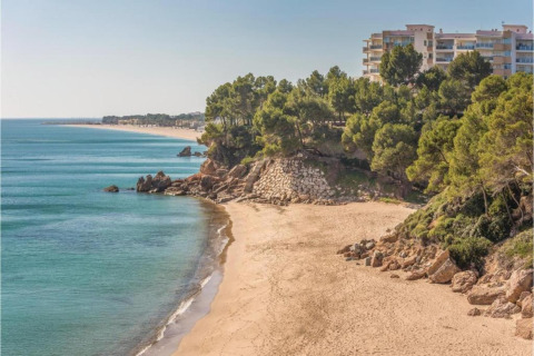 Vista sulla spiaggia sabbiosa, scogliere e case mobili a Torre del Sol, Spagna, tra alberi e mare azzurro.