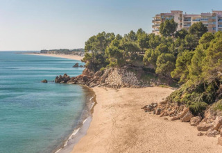 Udsigt over sandstrand, klipper og ferieboliger ved Torre del Sol i Spanien, omgivet af træer og blåt hav.