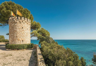 Torre in pietra con bandiere vicino al Mar Mediterraneo presso il mobilhome Torre del Sol Tent Pagan in Spagna, giornata soleggiata.