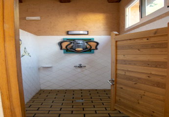 Salle de douche glamping avec carrelage, porte en bois et une tête d’éléphant originale comme pommeau.