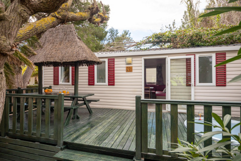 Mobilhjemmet Torre del Sol Cottage i Spanien med grøn veranda, stråtag og røde skodder.