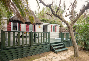 Mobil-home 'Torre del Sol Cottage' en Espagne avec terrasse verte, toit de chaume et végétation luxuriante.