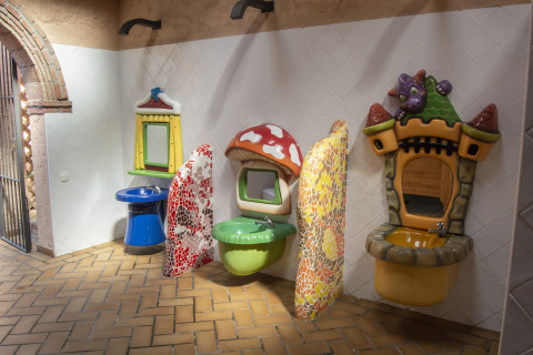 Baño infantil en glamping con lavabos coloridos y decoraciones temáticas de fantasía en las paredes.