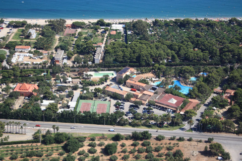 Vista aérea de un alojamiento glamping con piscina, canchas de tenis, estacionamiento y playa cercana.