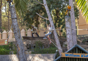 Area glamping a tema pirati con statue, corde sospese, palme e cartelli decorativi nell’ambiente naturale.