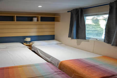 Habitación del Torre del Sol COTTAGE ACACIA en España, con tres camas individuales, mantas coloridas y ventana.