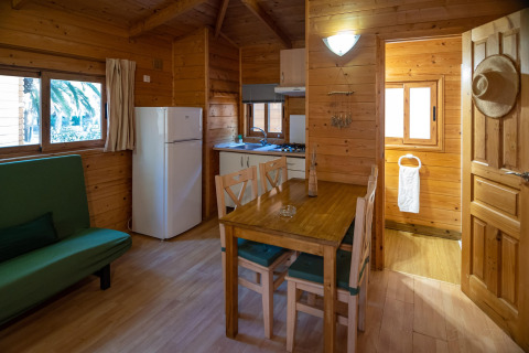 Vista interior de una cabaña de madera con cocina, mesa de comedor y sofá en TORRE DEL SOL Chalet Melia, España.