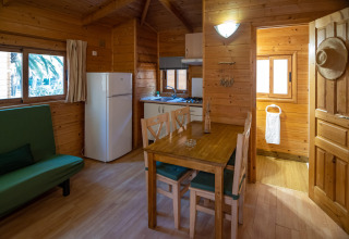 Vista interior de una cabaña de madera con cocina, mesa de comedor y sofá en TORRE DEL SOL Chalet Melia, España.