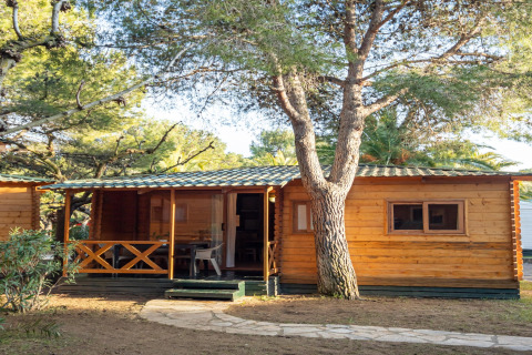 Cabaña de madera en TORRE DEL SOL Chalet Melia rodeada de árboles y luz solar, vista exterior con porche.