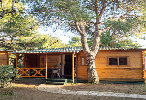 Cabaña de madera en TORRE DEL SOL Chalet Melia rodeada de árboles y luz solar, vista exterior con porche.