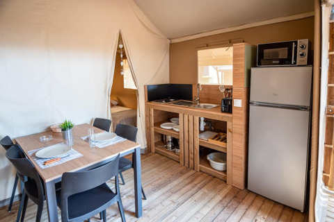 Interior of Torre del Sol TIENDA SAVANNAH safari tent in Spain, showing dining area, bed, and kitchenette.