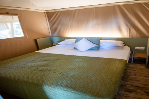 Camera da letto nella tenda safari Torre del Sol TIENDA SAVANNAH in Spagna con copriletto verde e pavimento in legno.