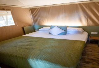 Bedroom inside the Torre del Sol TIENDA SAVANNAH safari tent in Spain with a green bedspread and wood floor.