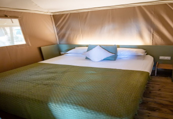 Camera da letto nella tenda safari Torre del Sol TIENDA SAVANNAH in Spagna con copriletto verde e pavimento in legno.