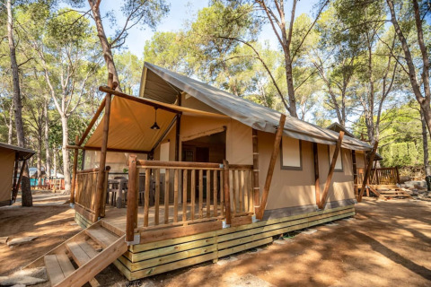 Safari tent at Torre del Sol in Spain, surrounded by trees, wooden porch and steps leading to entrance.