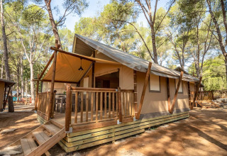 Safari tent at Torre del Sol in Spain, surrounded by trees, wooden porch and steps leading to entrance.