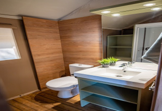 Modern bathroom with wooden walls, white fixtures and spacious sink in Torre del Sol Savannah safari tent, Spain.