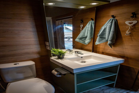 Bagno moderno alla Torre del Sol TIENDA SAVANNAH, Spagna, con lavandino, WC, specchio e asciugamani su parete in legno.
