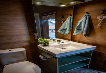 Bagno moderno alla Torre del Sol TIENDA SAVANNAH, Spagna, con lavandino, WC, specchio e asciugamani su parete in legno.