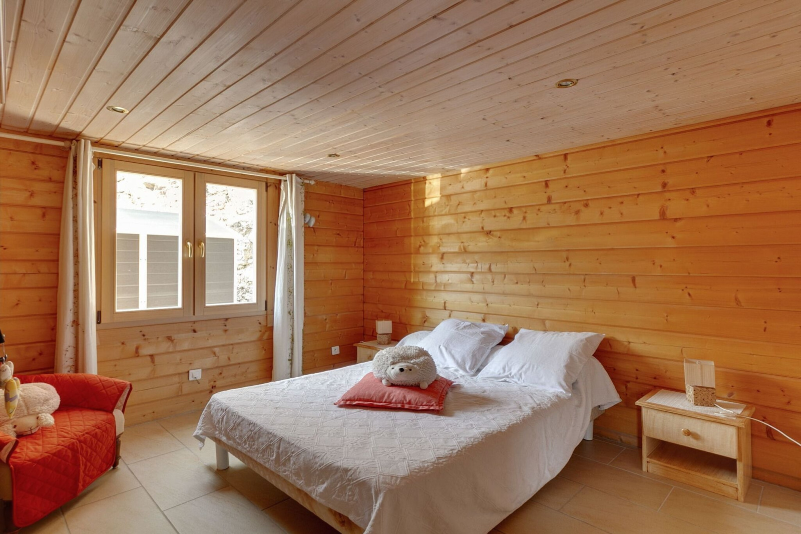 Gezellige slaapkamer in Chalet «Cheylard», Frankrijk, met houten muren, tweepersoonsbed en raam.