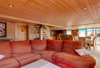 Accogliente soggiorno Chalet «Cheylard» in Francia con divano rosso, soffitto in legno e luce naturale.