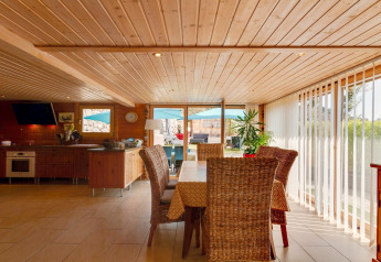 Zona pranzo e cucina luminosa nello Chalet Cheylard, Francia, con soffitto in legno e grandi finestre.