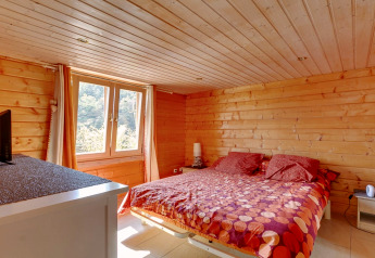 Camera da letto dello Chalet Cheylard in Francia con pareti in legno, letto matrimoniale e finestra sulla natura.