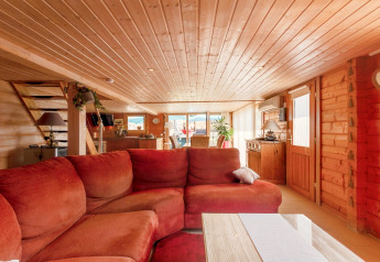 Soggiorno dello chalet «Cheylard» in Francia con rivestimenti in legno, divano rosso e ampie finestre.