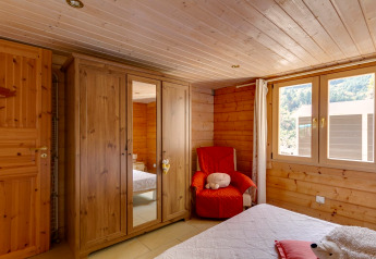 Camera da letto dello Chalet «Cheylard» in Francia, rivestita in legno, armadio e vista sulle montagne.