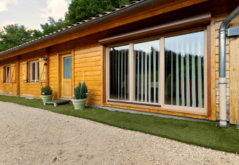 Vista esterna dello Chalet Cheylard in Francia con facciata in legno, grandi finestre e prato artificiale verde.