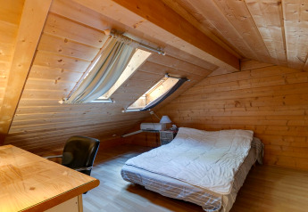 Camera mansardata allo Chalet «Cheylard» in Francia con pannelli in legno, scrivania e letto matrimoniale.
