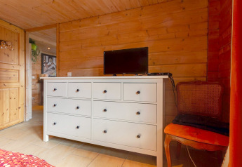 Camera da letto nello Chalet «Cheylard» in Francia con pareti in legno, cassettiera bianca, TV, sedia arancione.