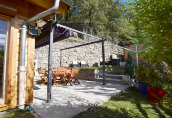 Terrazza esterna dello Chalet «Cheylard» in Francia con mobili in legno, muro in pietra e piante verdi.