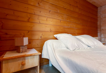 Camera da letto nello Chalet «Cheylard» in Francia, con pareti in legno, letto matrimoniale e comodino con lampada.