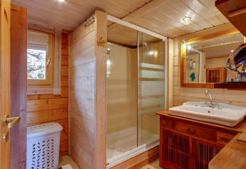 Bagno accogliente in legno con doccia in vetro e lavabo ampio nello Chalet Cheylard in Francia e illuminazione calda.