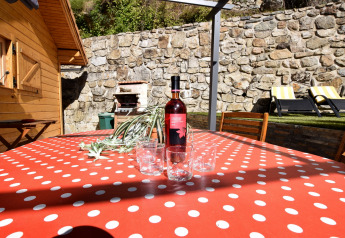 Terrazza soleggiata dello Chalet «Cheylard» in Francia con tavolo a pois rossi, vino e bicchieri.
