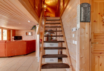Interno dello Chalet Cheylard in Francia, area soggiorno con divano arancione, pareti in legno e scala.