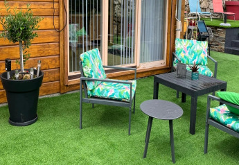 Patio esterno Chalet 'Cheylard', Francia, con arredi da giardino e prato sintetico davanti a parete in legno.