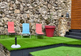 Patio esterno presso Chalet «Cheylard» in Francia con sedie colorate, prato artificiale e muro di pietra.