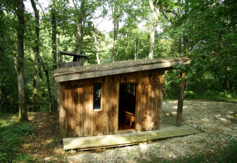 Wooden cabin named Ecolodge en Sequoia in a forest, with sloped roof and small deck surrounded by trees.