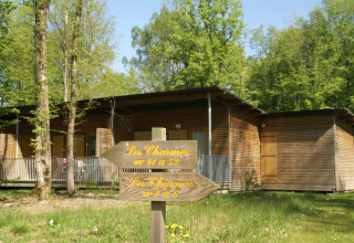 Foto van een houten lodge te midden van bomen, met wegwijzers naar verschillende kamers in het bos.