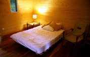 Cozy wooden bedroom at Ecolodge «en Sequoia» in France, featuring a bed, chair and warm lighting.
