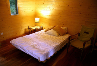 Cozy wooden bedroom at Ecolodge «en Sequoia» in France, featuring a bed, chair and warm lighting.